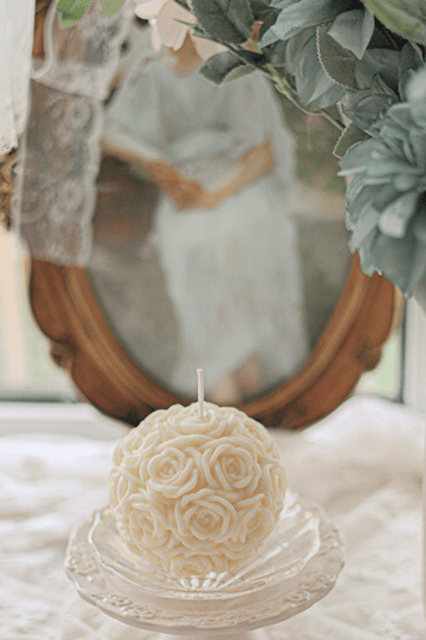 Round rose-shaped candle on lace tablecloth. | Rund rosformad ljus på spetsduk.