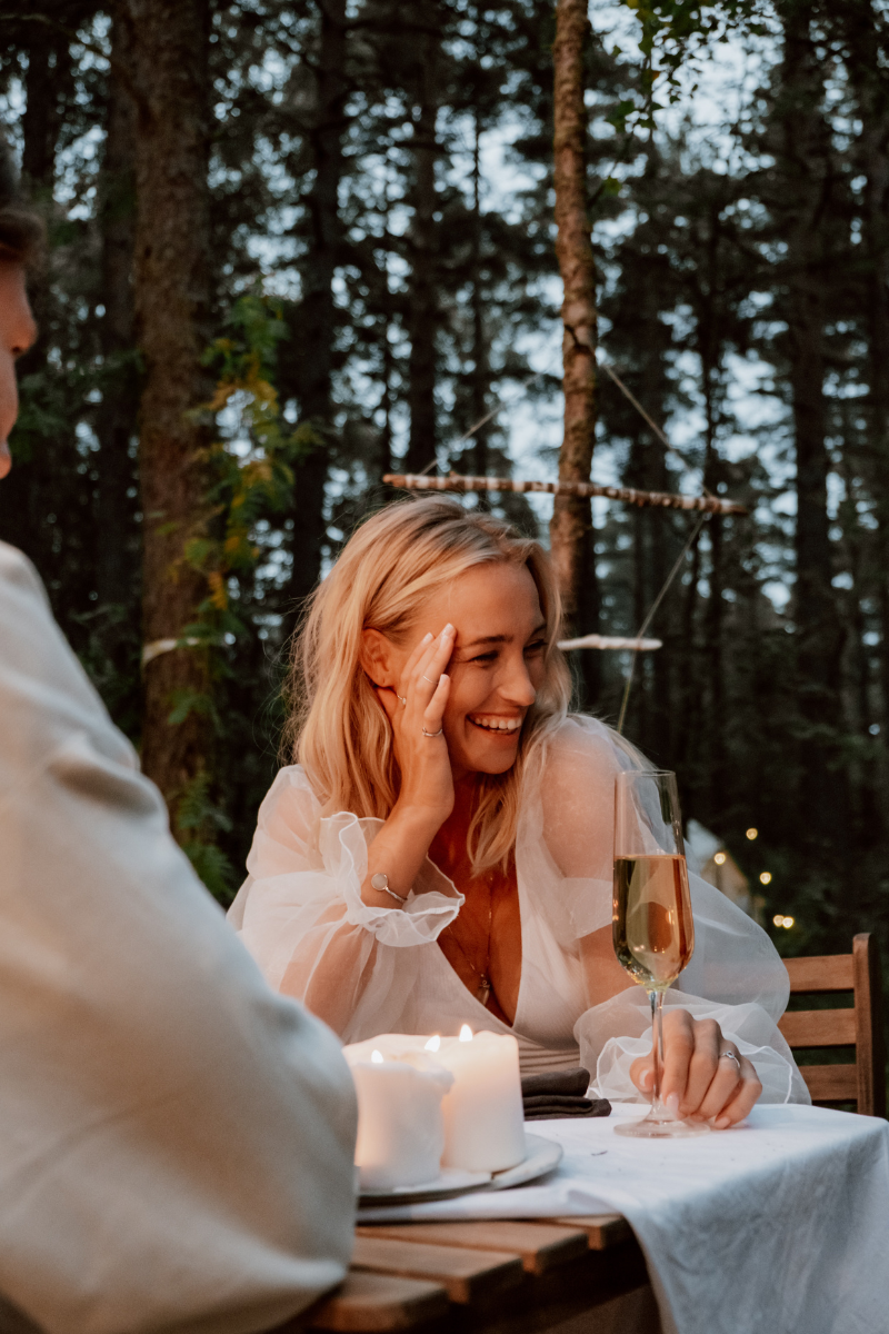 Woman laughing with a glass of wine in a forest, embodying joyful relaxation