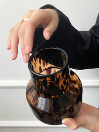 Small glass vase, leopard texture, in hand of a woman. | Liten glasvas, leopardtextur, i kvinnas hand.