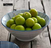 reen apples in blue-lined bowl on wooden table." | Gröna äpplen i blåfodrad skål på träbord.