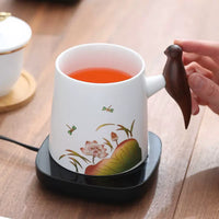 White cup with tea being heated, wooden magpie handle. | Vit kopp med te som värms, träskatthandtag