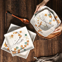 Hands setting square plates with Japanese designs." | Händer lägger kvadratiska tallrikar med japanska mönster.