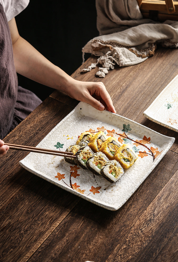 Sushi rolls on square plate, maple leaf patterns." | Sushi-rullar på kvadratisk tallrik, lövmönster.