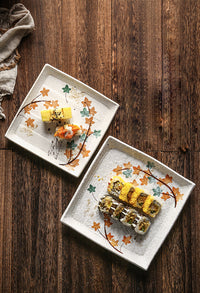 Sushi rolls on two square plates, autumn leaf patterns." | Sushi-rullar på två kvadratiska tallrikar, höstlövmönster.