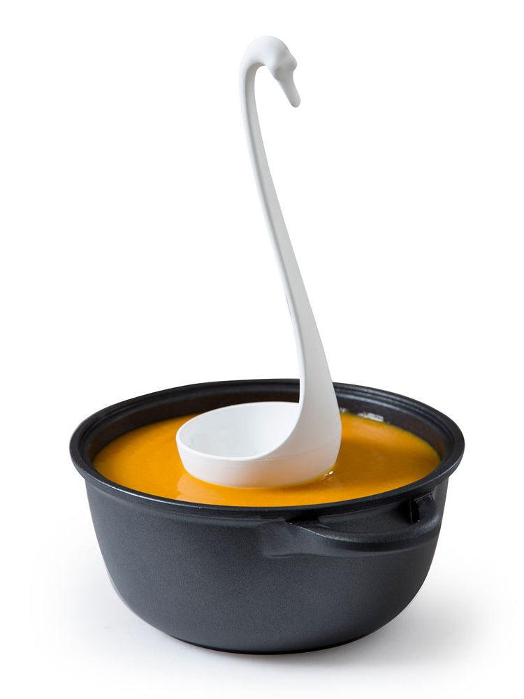 Graceful black swan ladle in vibrant orange soup, sleek black bowl. | Graciös svart svanformad slev i levande orange soppa, stilren svart skål