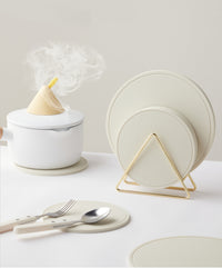 Set of white trivet mats in golden triangle, kitchen setting. | Set vita grytunderlägg i gyllene triangel, köksmiljö.