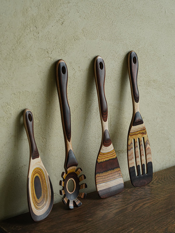 Handcrafted wooden utensils displaying rich, dark, and light brown grain patterns, artfully arrayed against a textured cream background.