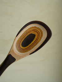 A detailed close-up showcasing the natural, concentric wood grain pattern on a finely crafted wooden spoon against a soft, off-white surface.